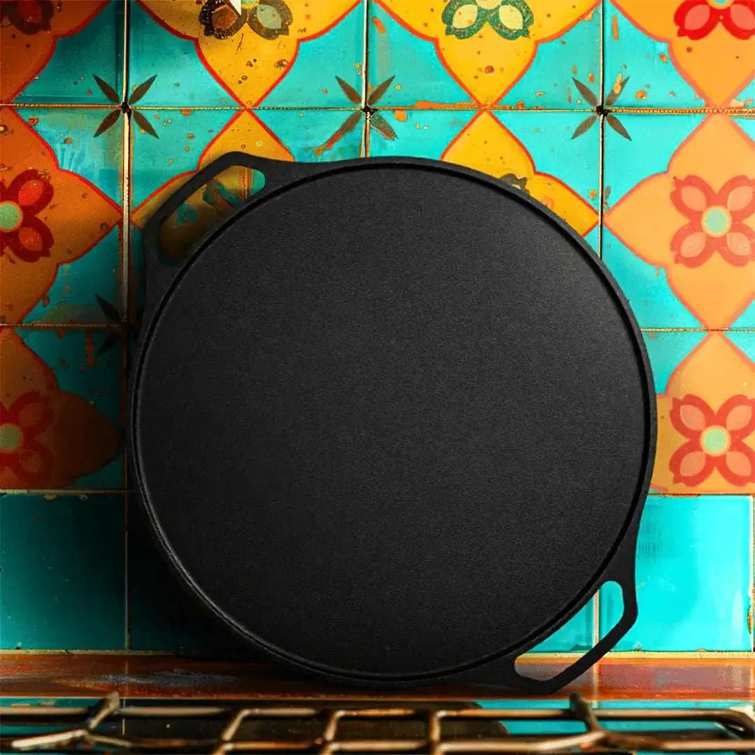 Roca Carpo 30cm cast iron dosa tawa with double handles on a colorful tiled background.