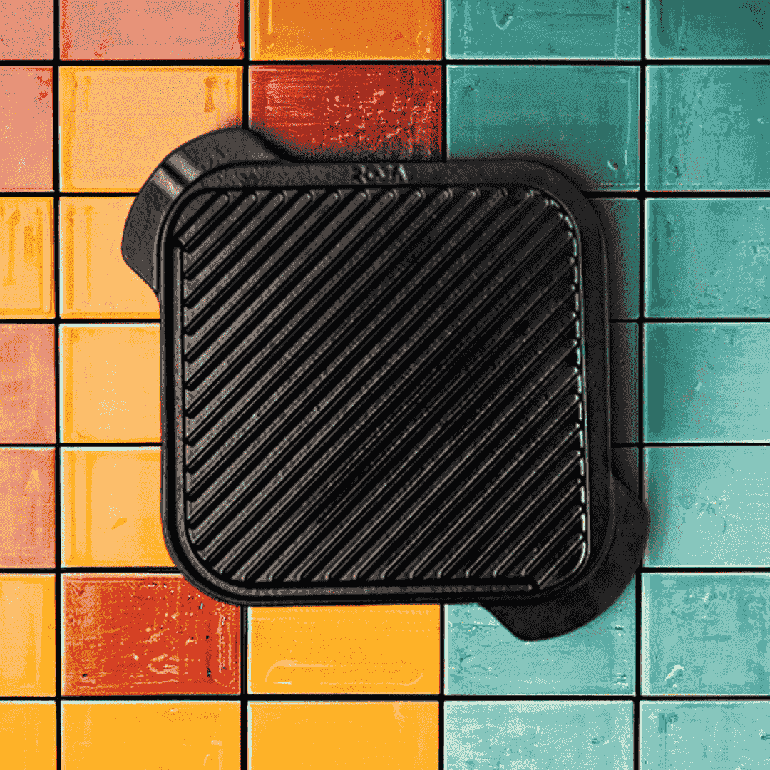 Square 20cm Roca Europa cast iron grill plate with ridged surface on a colorful tiled background.
