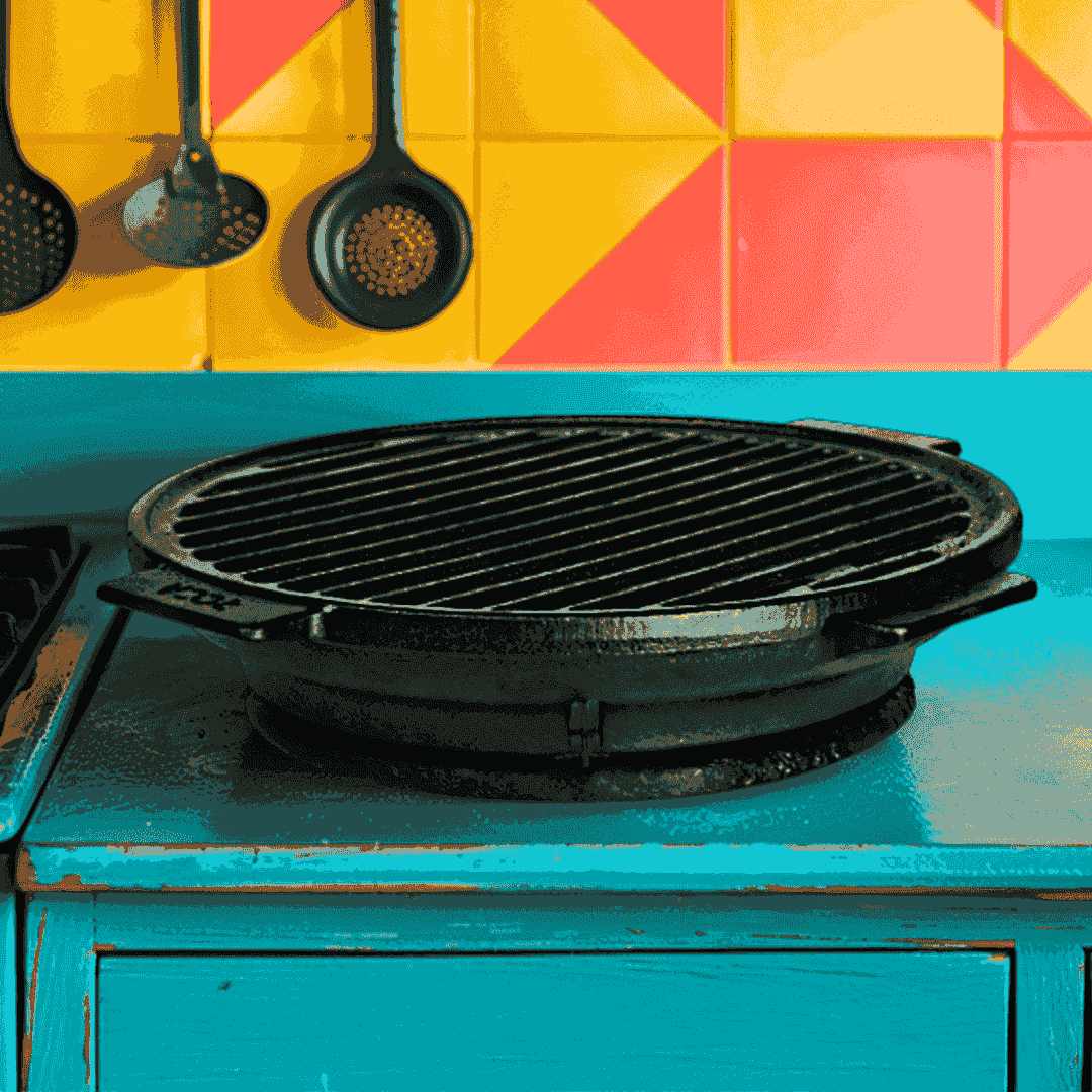 Round 24cm pre-seasoned cast iron stove grill with handles on a blue countertop.