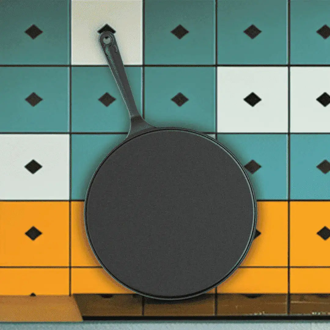 A dark gray cast iron skillet with a long handle, shown from a top-down angle against a colorful tiled background with teal, white, and orange squares.