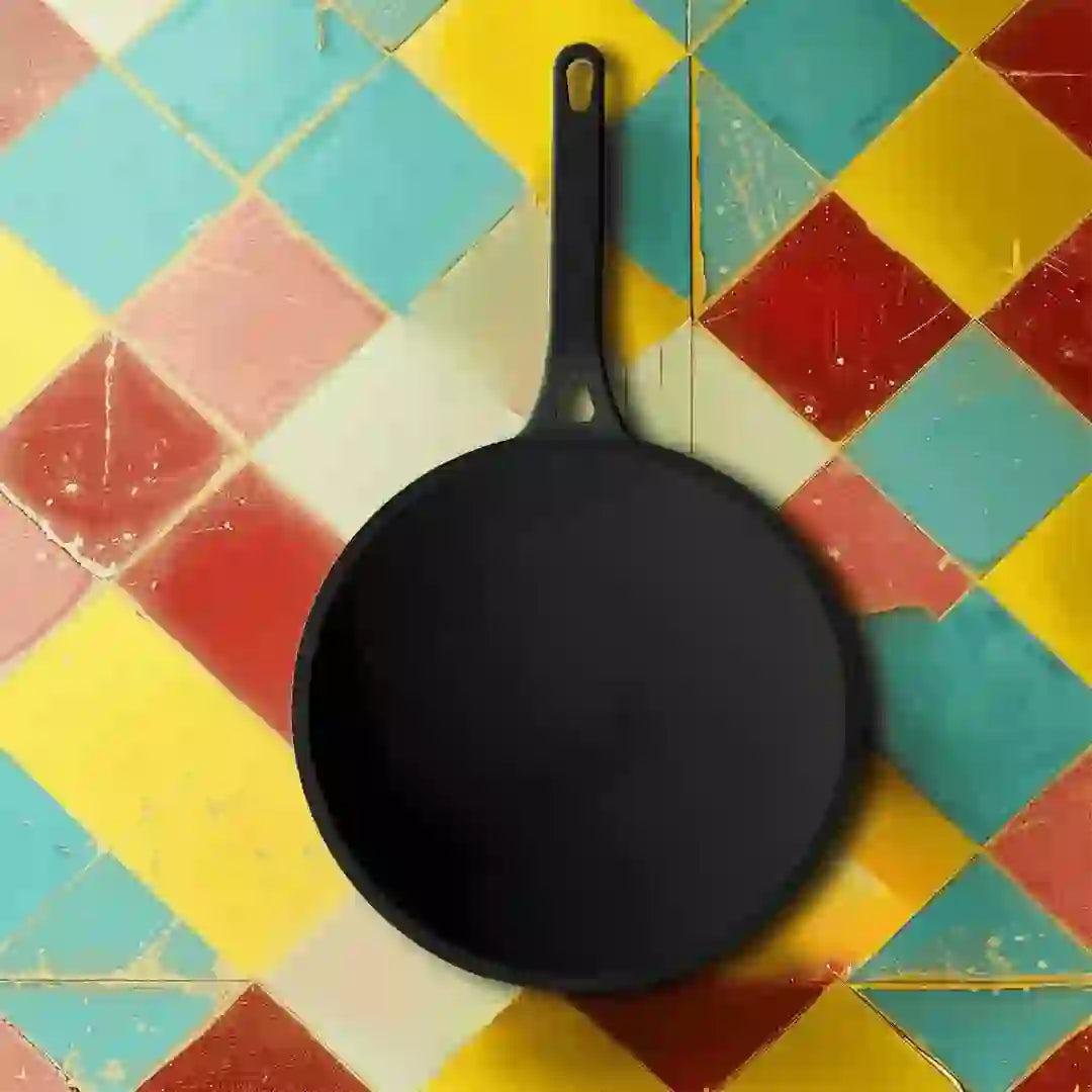 Roca Nix 26cm pre-seasoned cast iron roti tawa with long handle on a colorful tiled background.