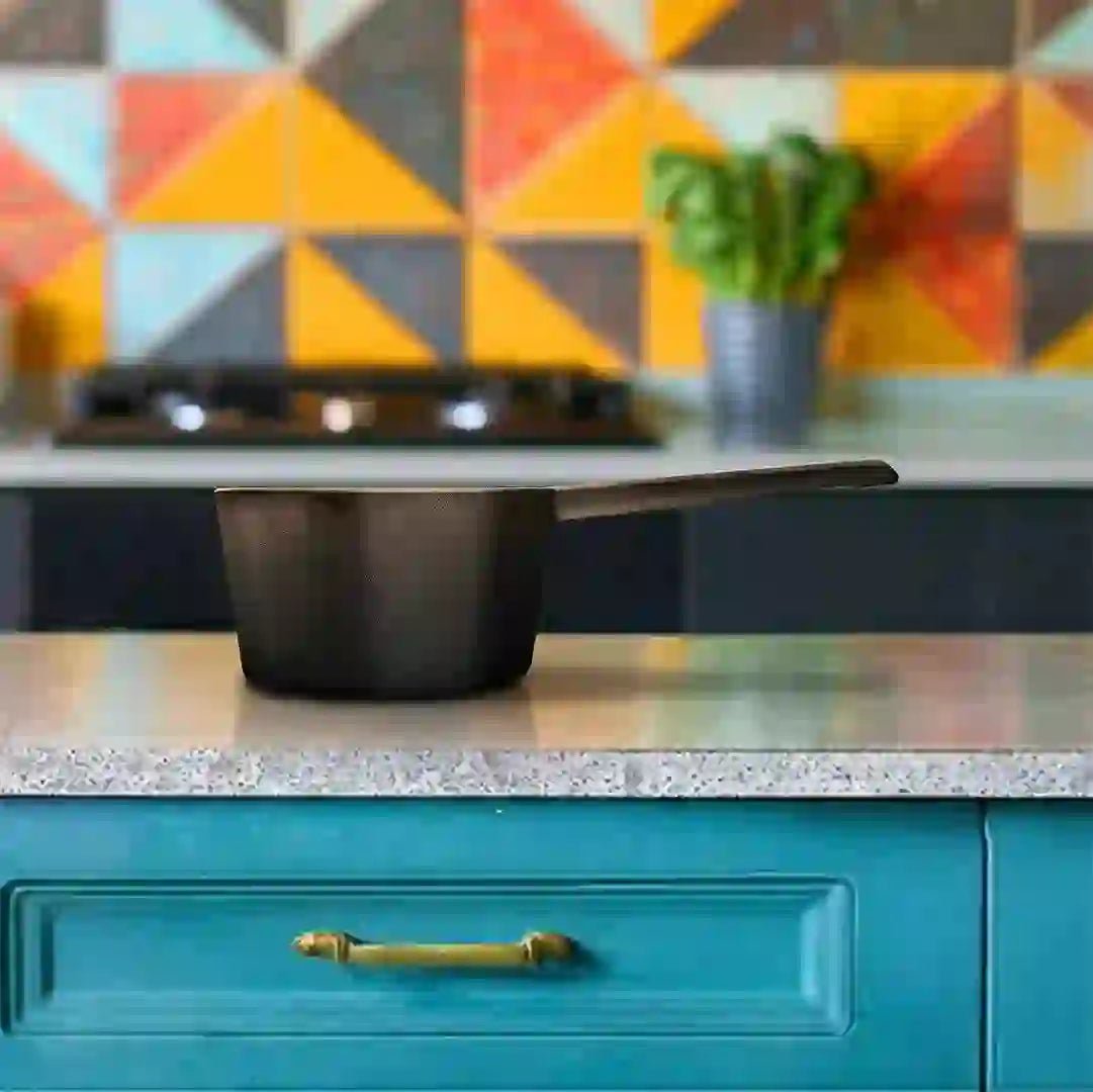 Roca Triton 11cm pre-seasoned cast iron sauce pan on a kitchen counter with a colorful tiled wall.
