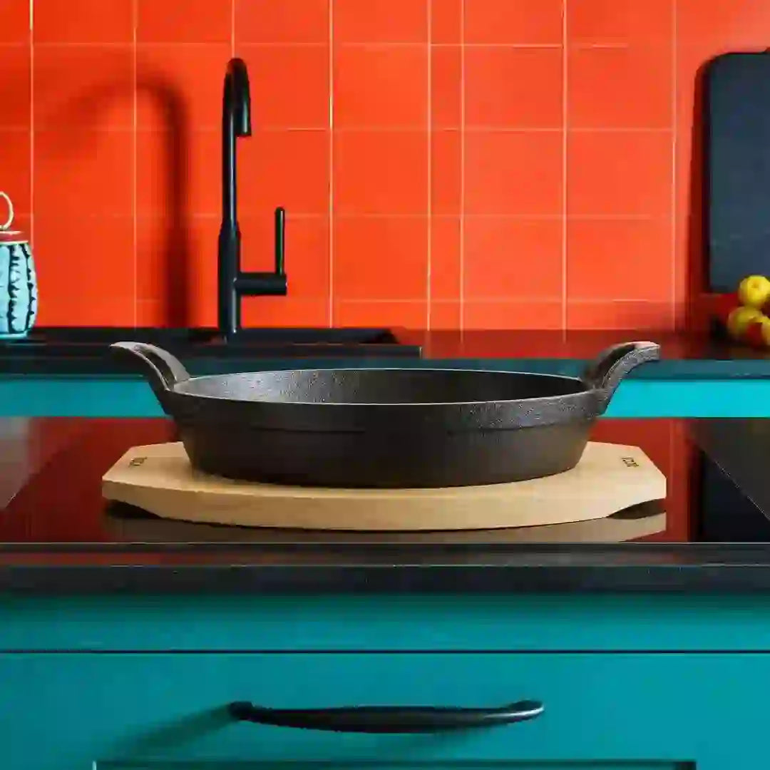 Roca Atlas cast iron oval pan on a wooden tray, set on a kitchen counter with orange tile background.