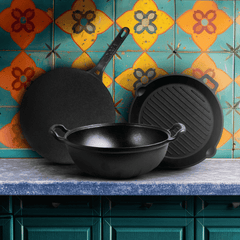Set of black cast iron cookware on a kitchen counter with colorful tiles in the background