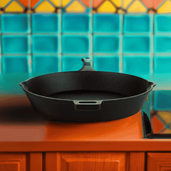 Black cast iron skillet on a wooden surface with a colorful tiled wall in the background