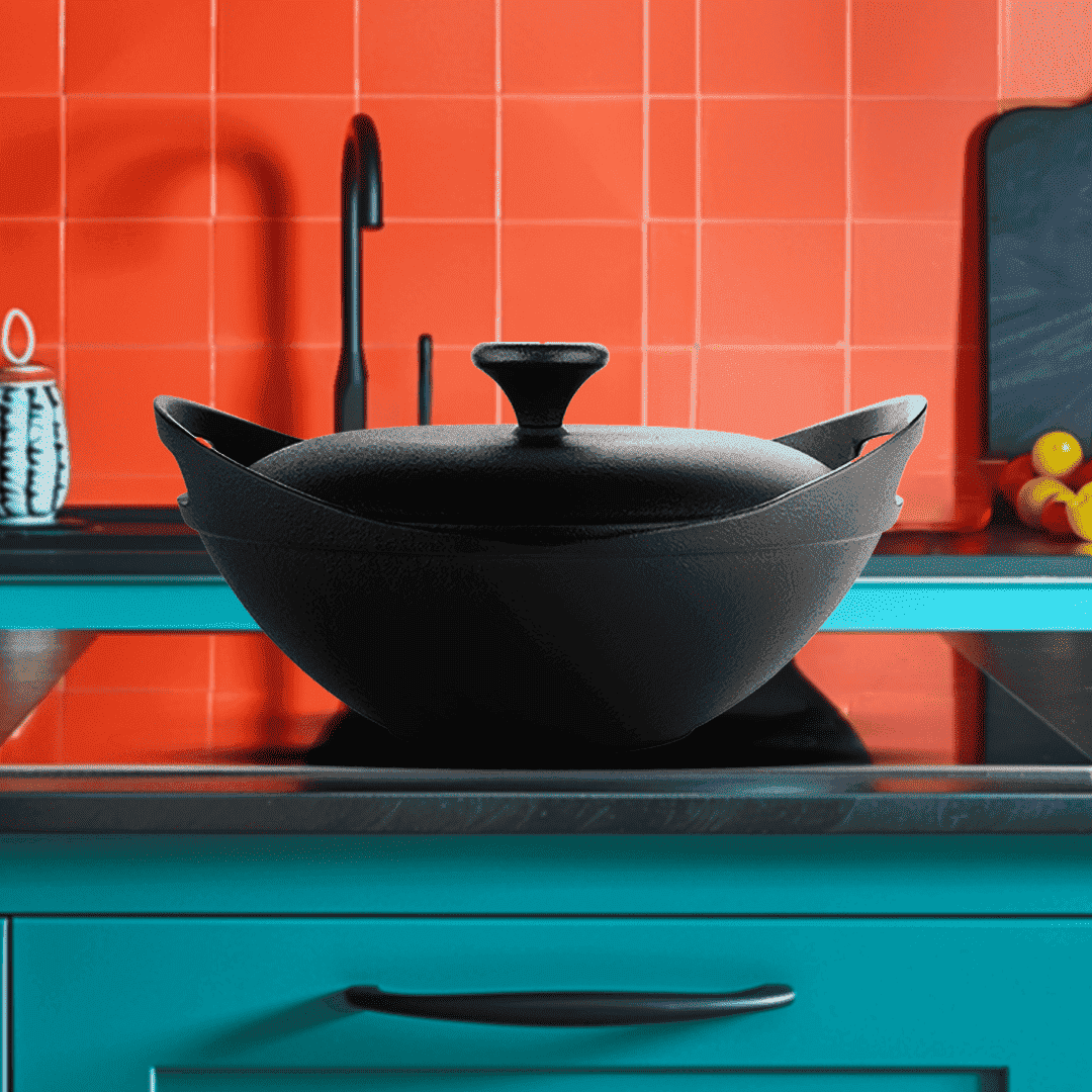 Black wok with lid on a stove against an orange tiled wall