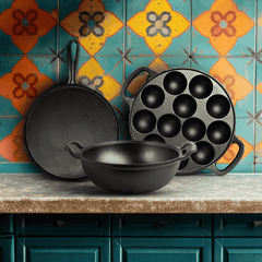 Roca cast iron set: 28cm dosa tawa, 12-pit paniyarakkal, and 24cm kadai on a kitchen counter.